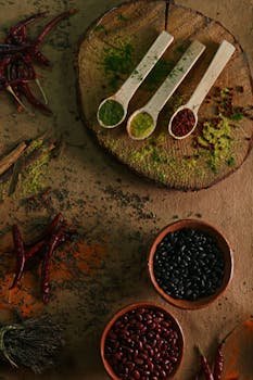 A top-down view of various spices and beans arranged on a rustic wooden surface for culinary art.