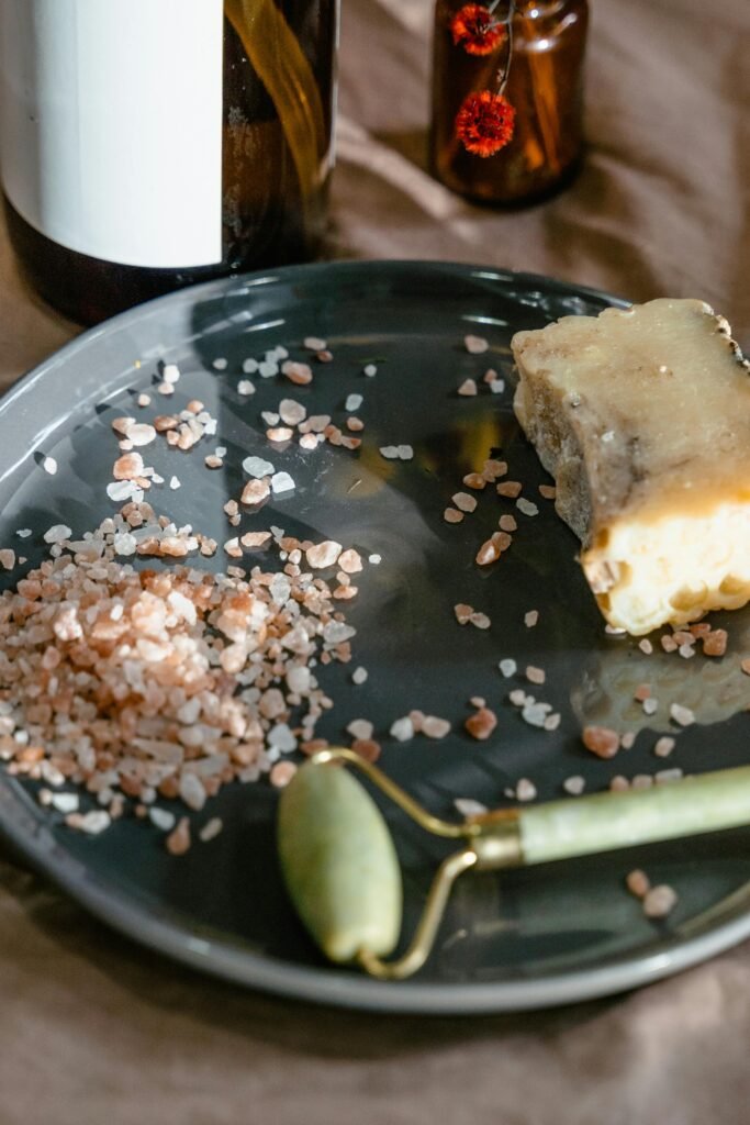 A collection of natural skincare items including rock salt and a jade roller on a ceramic plate.