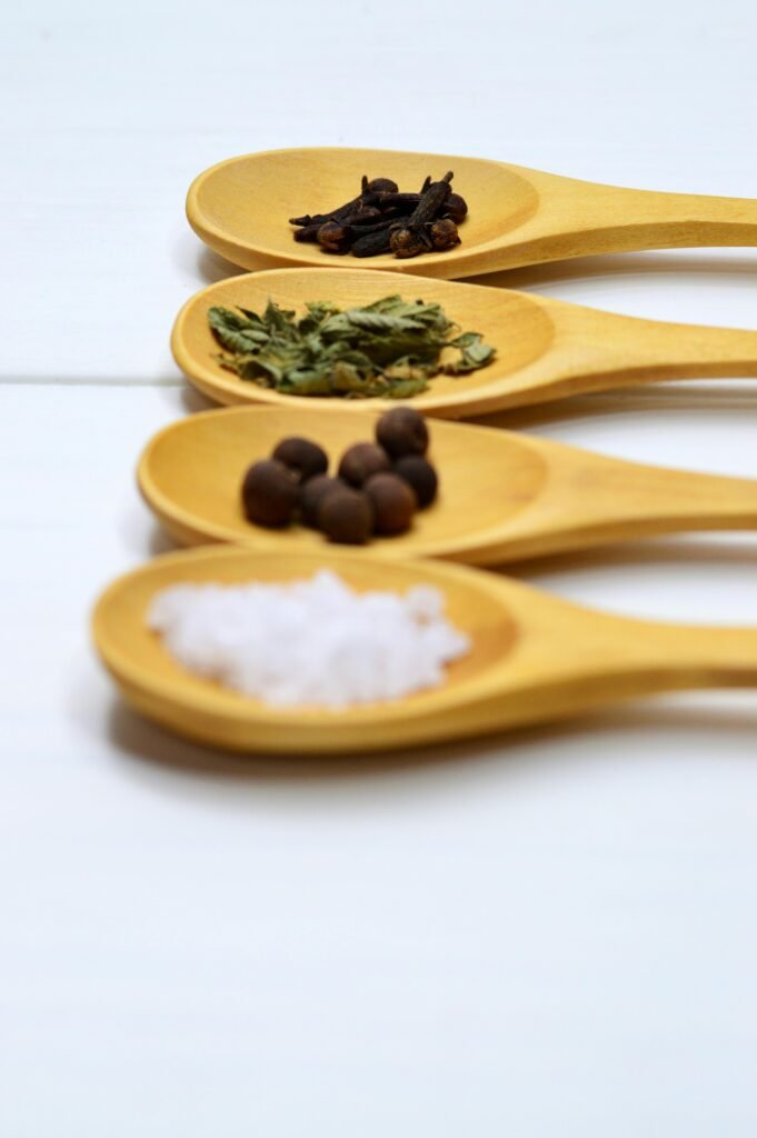 A variety of spices arranged neatly on wooden spoons over a white surface, providing culinary inspiration.